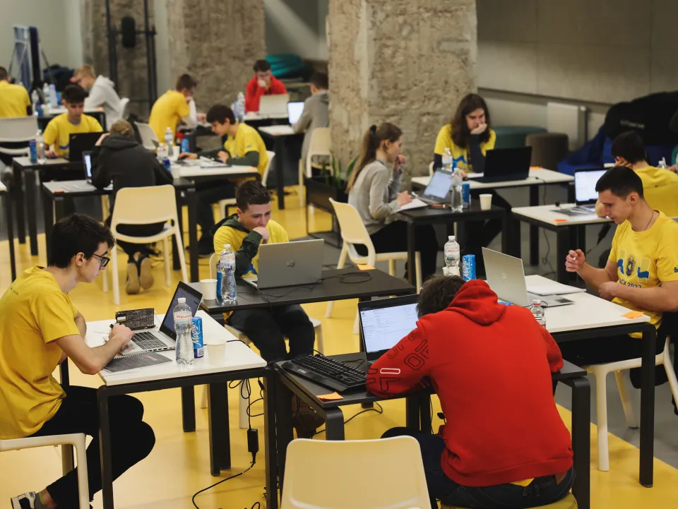 Finalists sitting a round at laptops on separate desks in a large hall with concrete columns